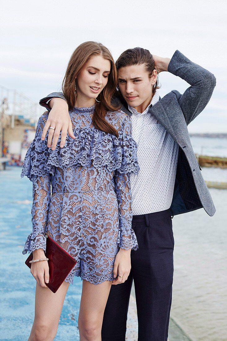 A young woman wearing a purple lace dress and a young man wearing a polka dot shirt and a green jacket