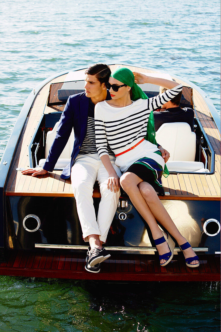 A young woman wearing a grey headscarf and a blue-and-white outfit sitting on a boat with young man also wearing a blue-and-white outfit