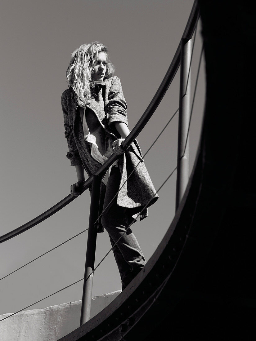 A young woman wearing a coat standing against a banister (black-and-white shot)