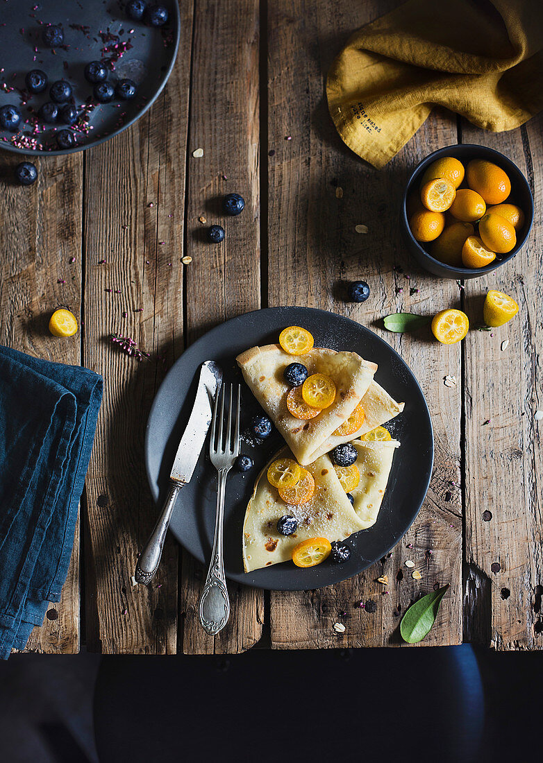 Crepes with blueberries and tangerines on wooden table