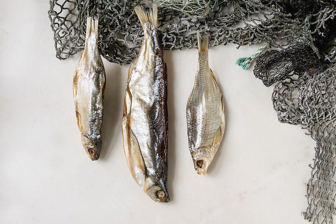 Dried fish or stockfish on fishing nets over white marble background