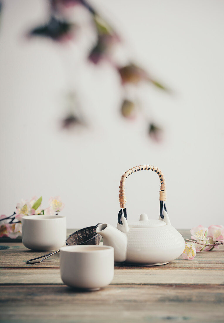 Stillleben mit weißer Teekanne, Teesieb, Teebechern und Kirschblüten
