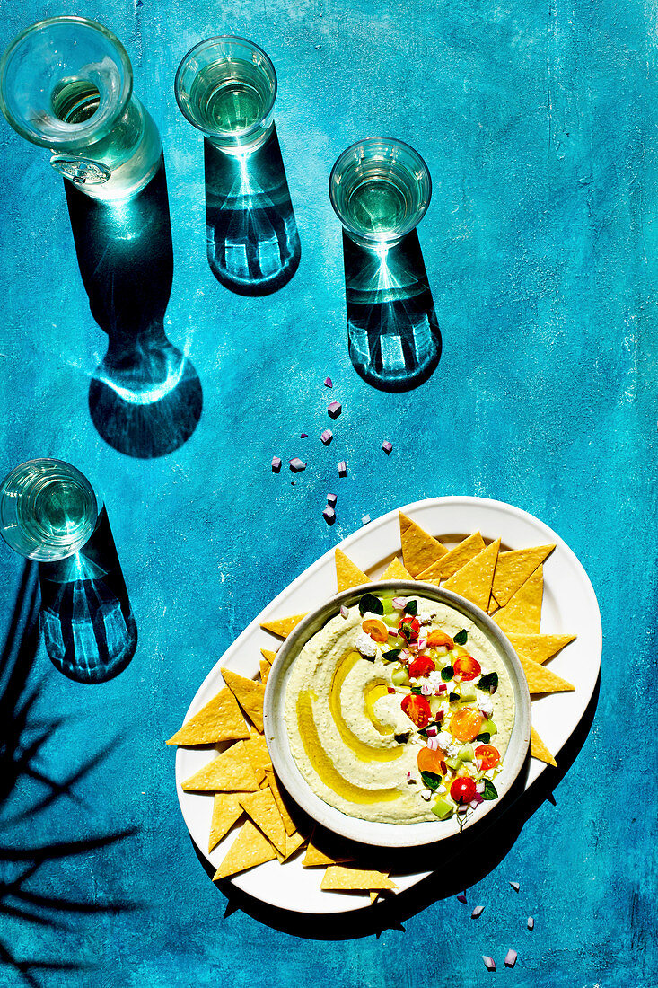 Oregano-Hummus mit Feta serviert mit Crackern auf blauem Untergrund