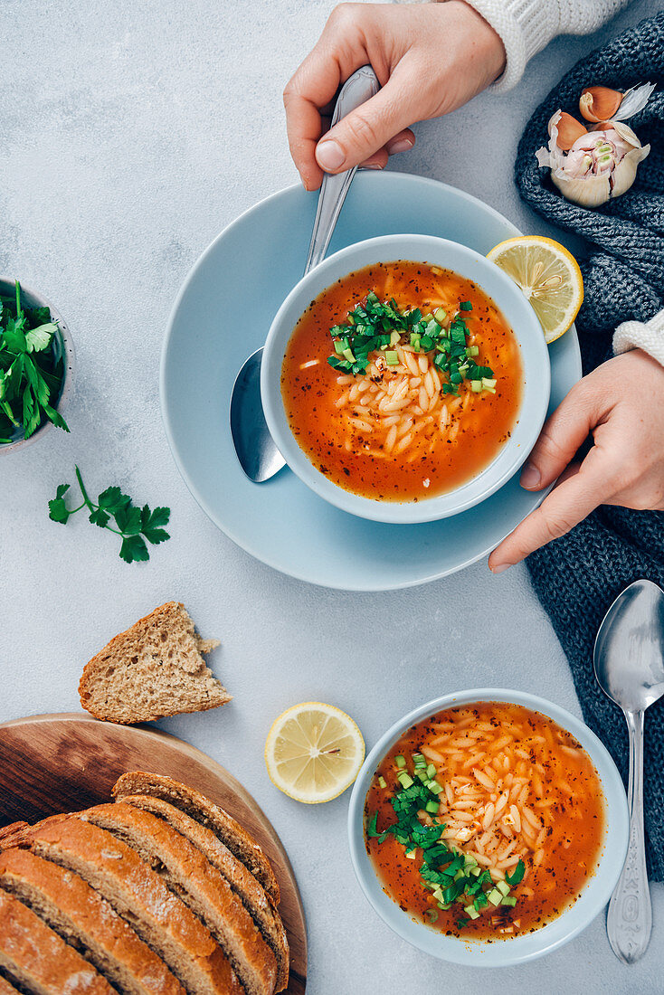 Woman eating Turkish tomato orzo soup garnished with parsley served