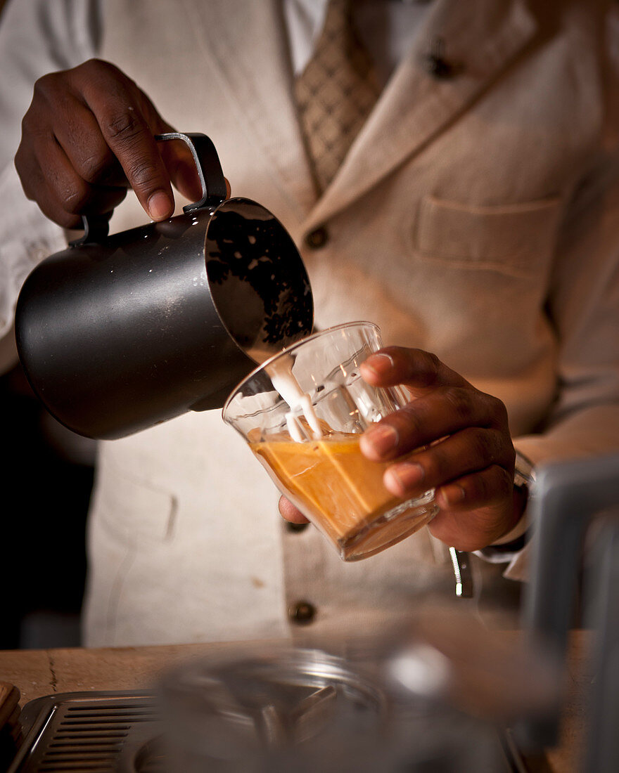 A barista pouring milk into a glass of coffee