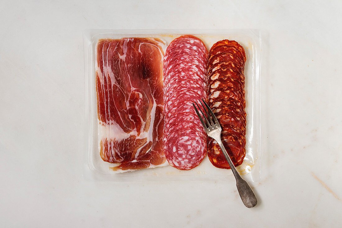 Antipasto meat platter assorti of sliced jamon, salami, chorizo sausage in opened plastic packaging