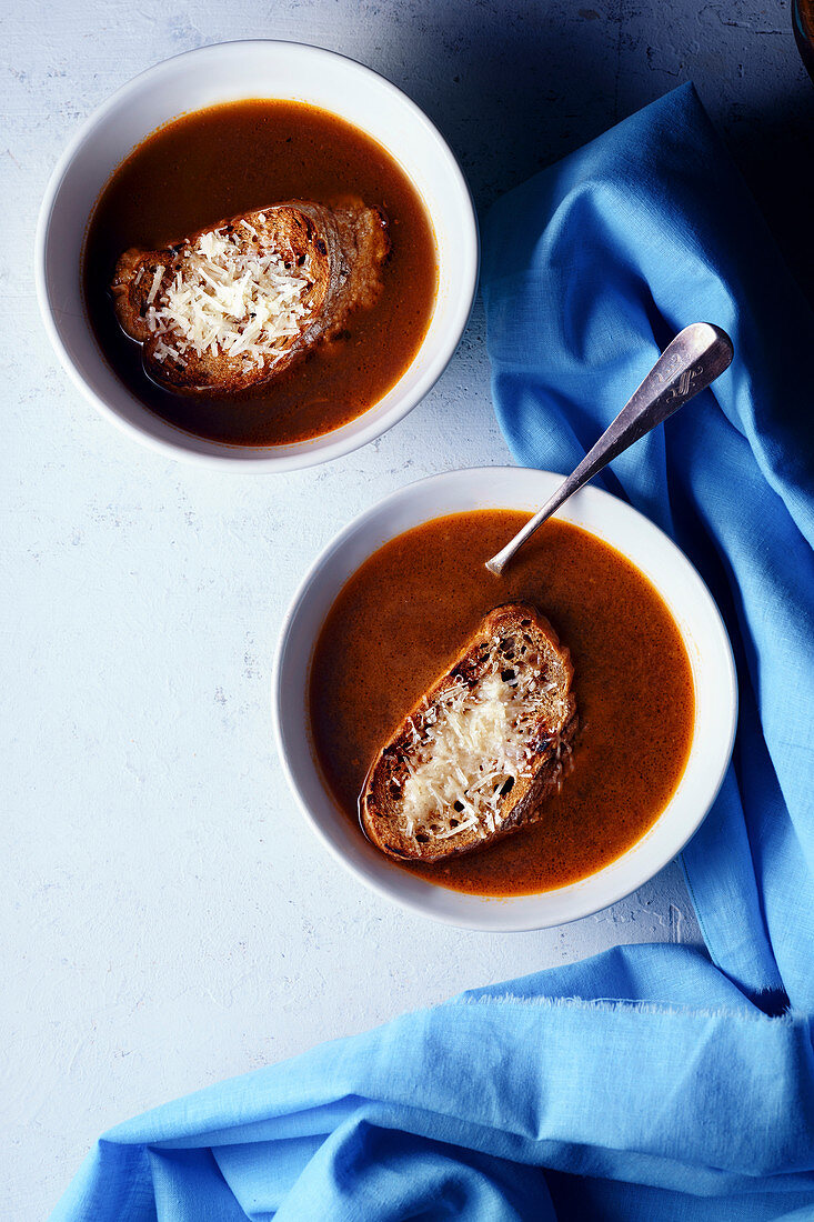 Two bowls of hot vegetarian soup served with croutons and parmesan