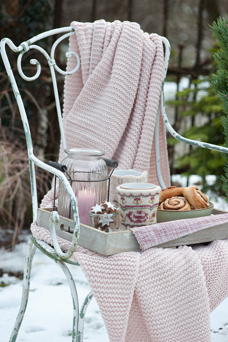 Tray with a lantern, pastries, and cups on a chair with a blanket