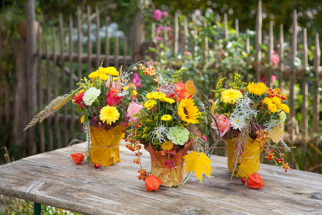 Bouquets of sunflowers and chrysanthemums in vases covered in autumn leaves