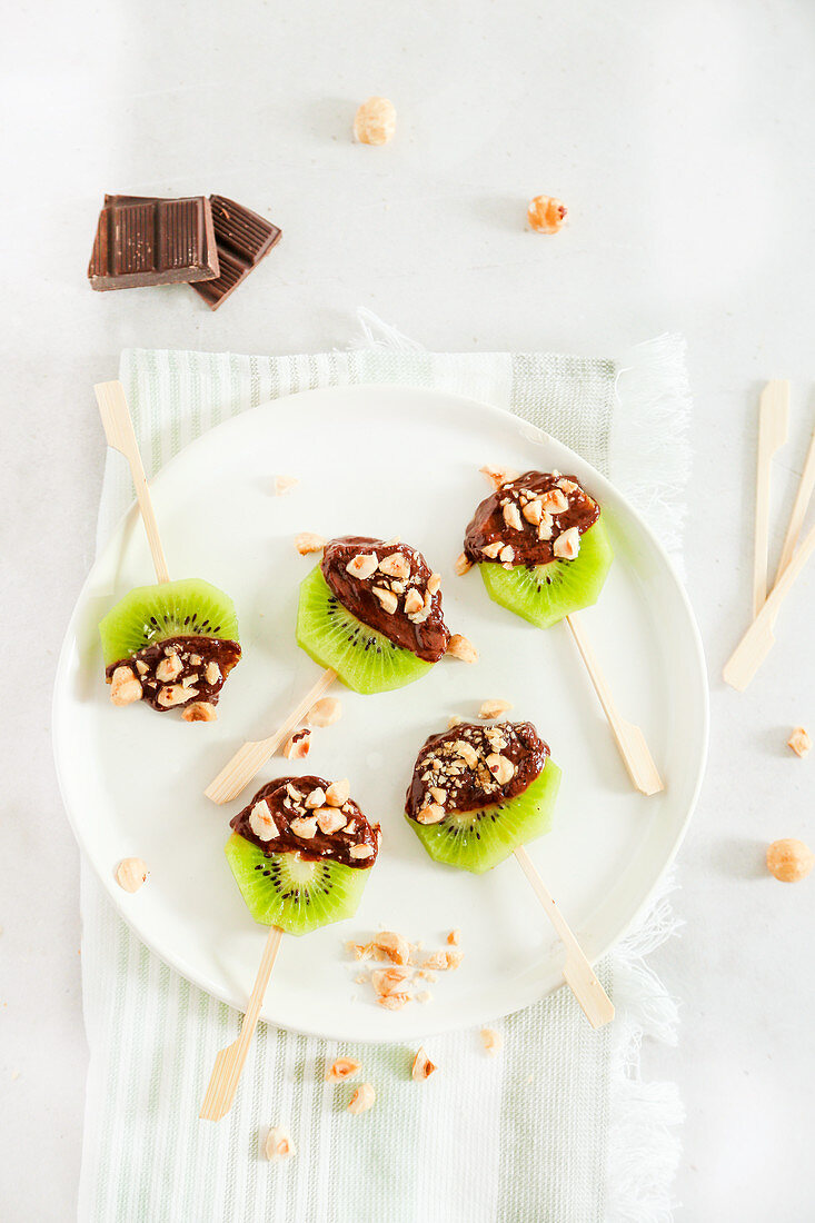 Kiwi lollipops with melted chocolate and chopped hazelnuts