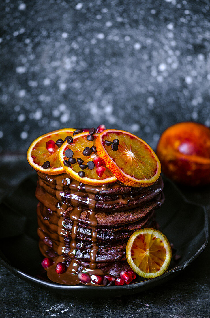 Chocolate pancakes with chocolate drops, sprinkled with chocolate sauce, decorated with slices of red oranges