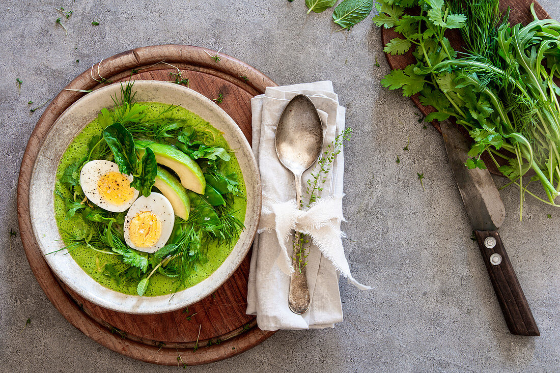 A smoothie bowl with boiled egg, avocado and mange tout in a nest of herbs