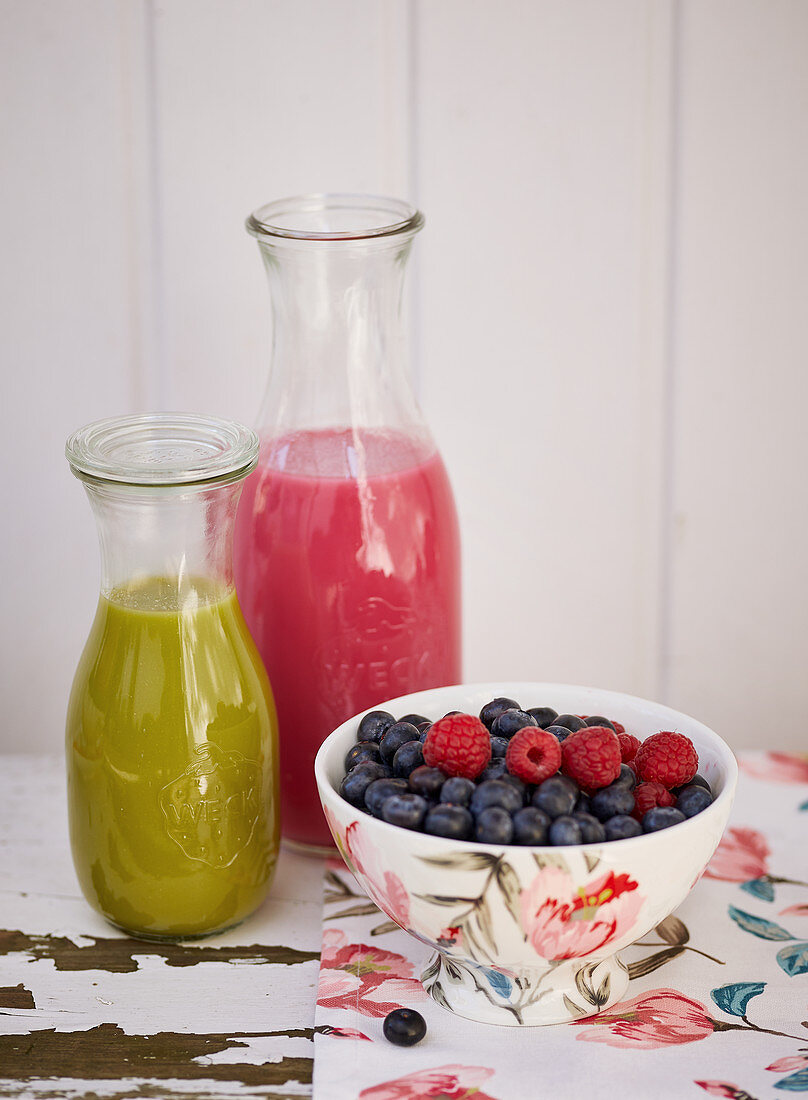 Two smoothies in bottles next to a smoothie muesli bowl