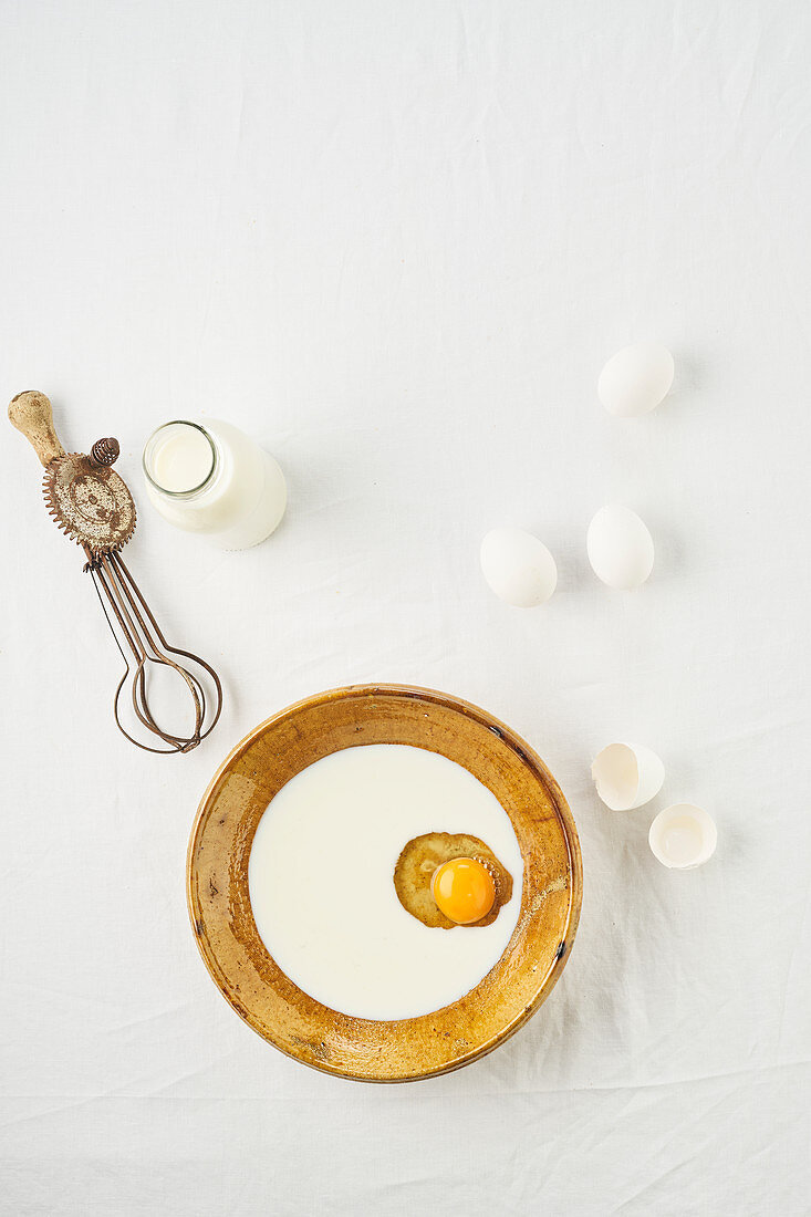 An egg cracked in a bowl of milk