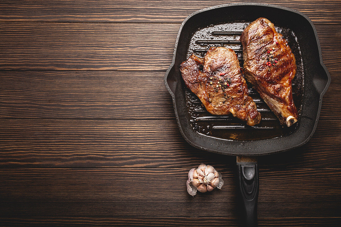 Two seared rib-eye steaks in a pan on a wooden surface
