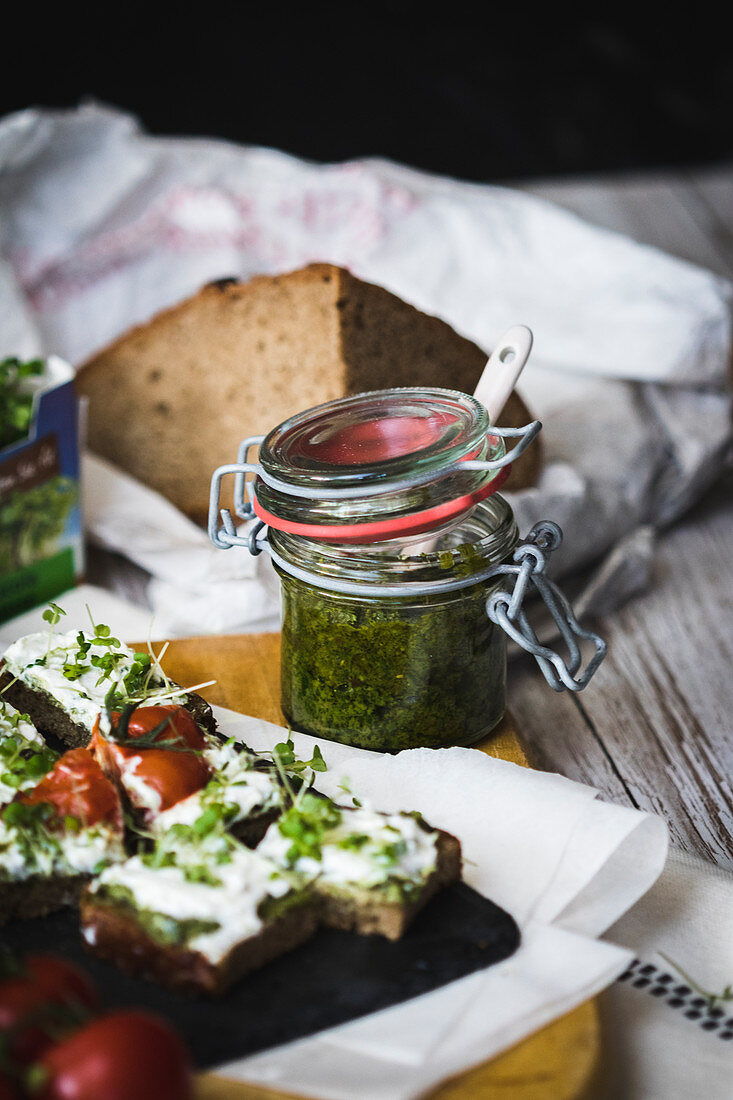 Pesto in a flip-top jar with a slice of bread topped with cream cheese and cress