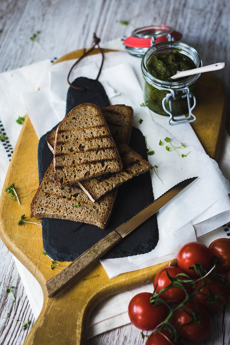 Getoastetes Bauernbrot, daneben Tomaten und Pesto