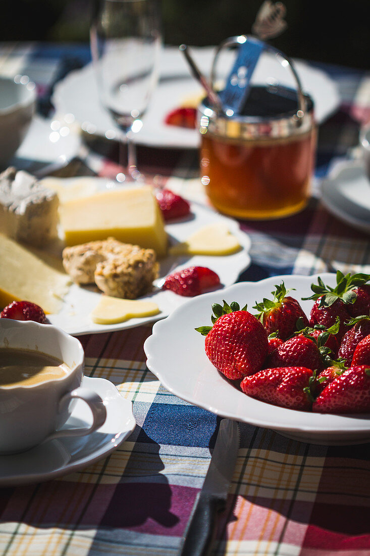 Frühstückstisch im Freien mit Kaffee, Erdbeeren, Käseteller und Marmelade