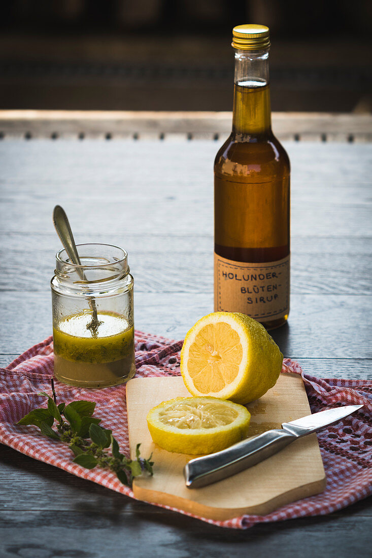 A bottle of elderflower syrup behind a sliced lemon on a wooden surface