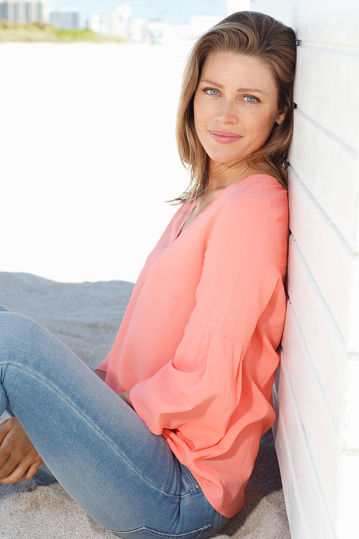 A young woman on a beach wearing an apricot blouse and jeans