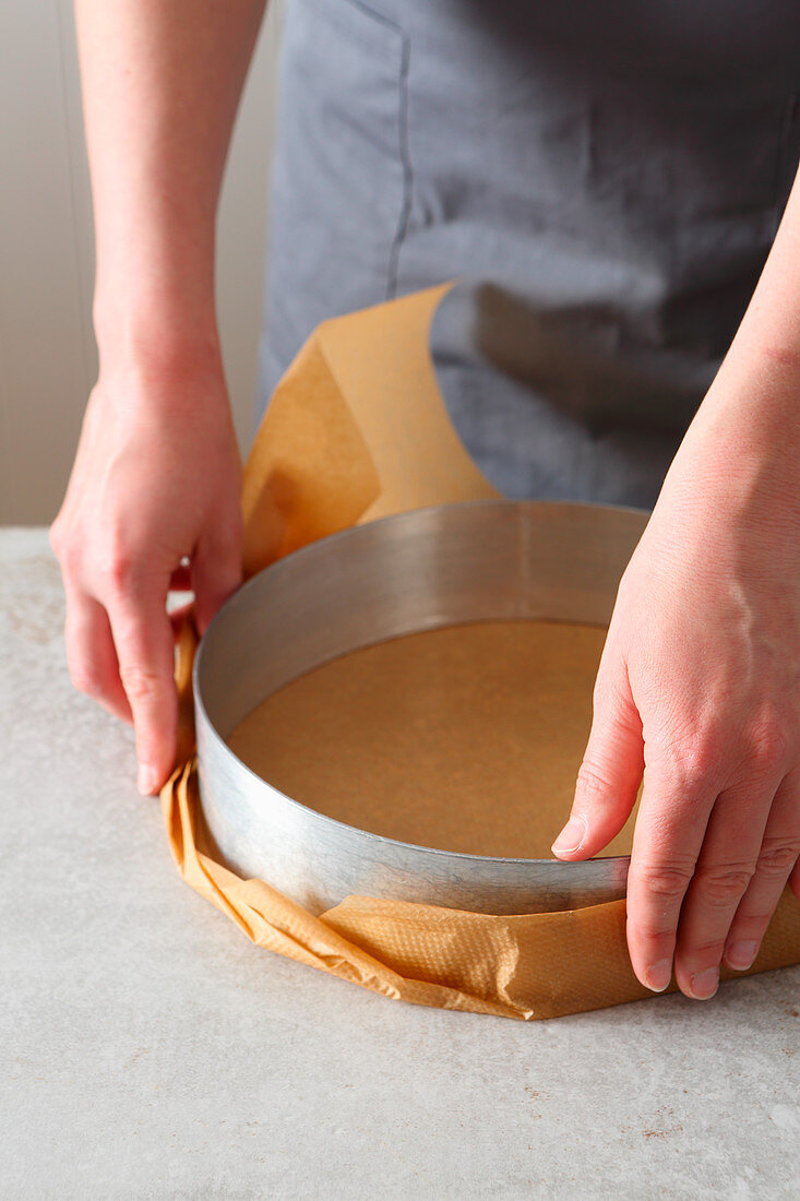 A cake ring being wrapped in baking paper
