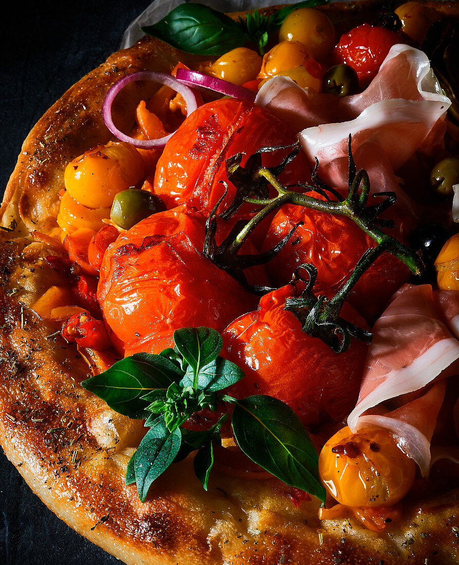 A pizza topped with tomatoes, ham and olives (close-up)