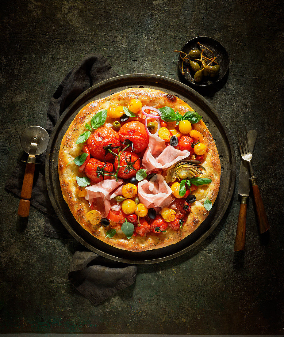 Pizza mit Tomaten, Schinken und Kapernäpfeln