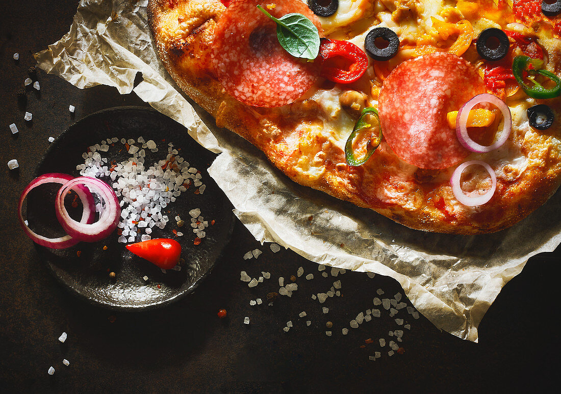 A pizza topped with salami, olives, peperoni and onions (close-up)