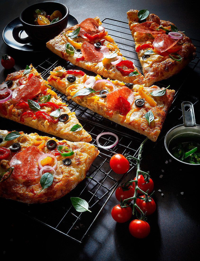 Pizza mit Salami, Tomaten und Oliven, in Stücke geschnitten
