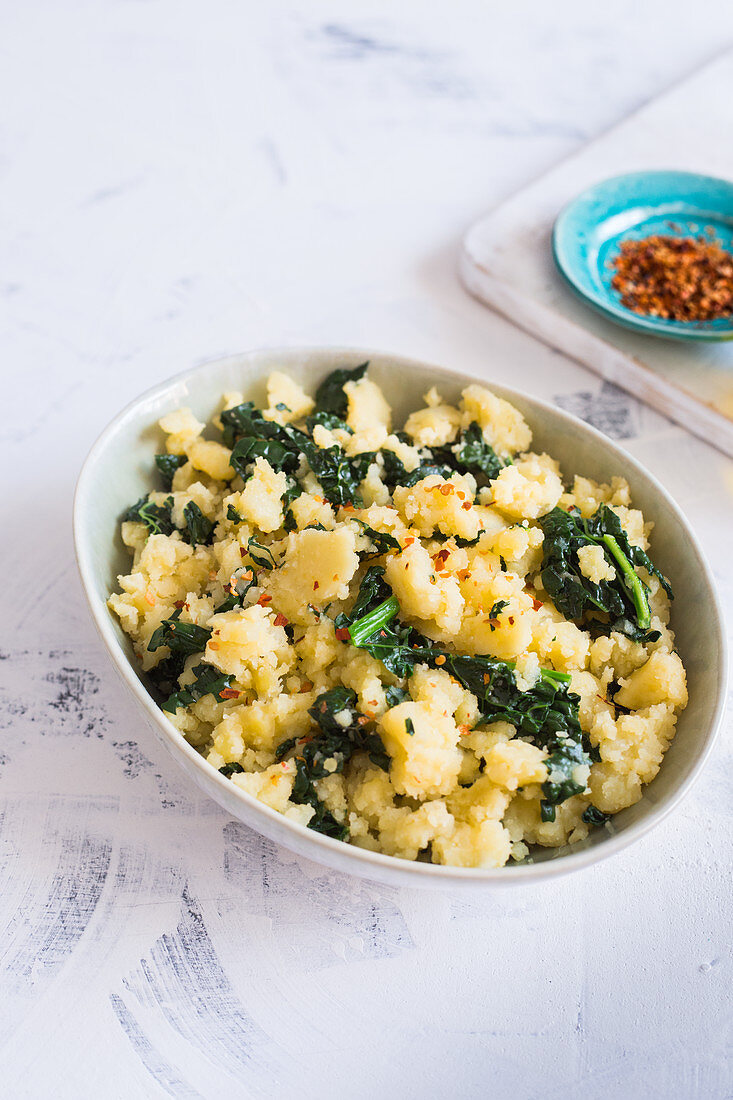 A bowl containing mashed potatoes with kale, chilli flakes and olive oil, vegan dish