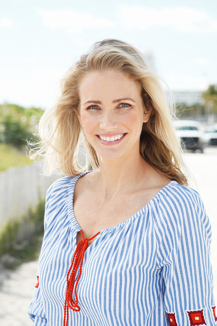 A blonde woman outside wearing a blue-and-white striped blouse
