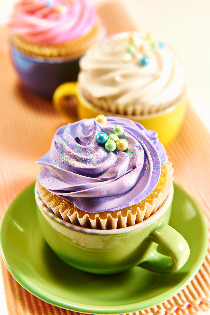 Cupcakes decorated with different coloured buttercream served in colourful tea cups