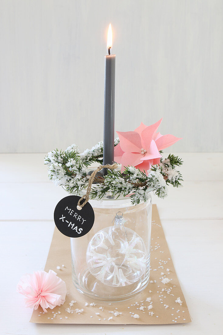 Christmas-tree bauble in jar decorated with fir sprigs and tag used as candlestick