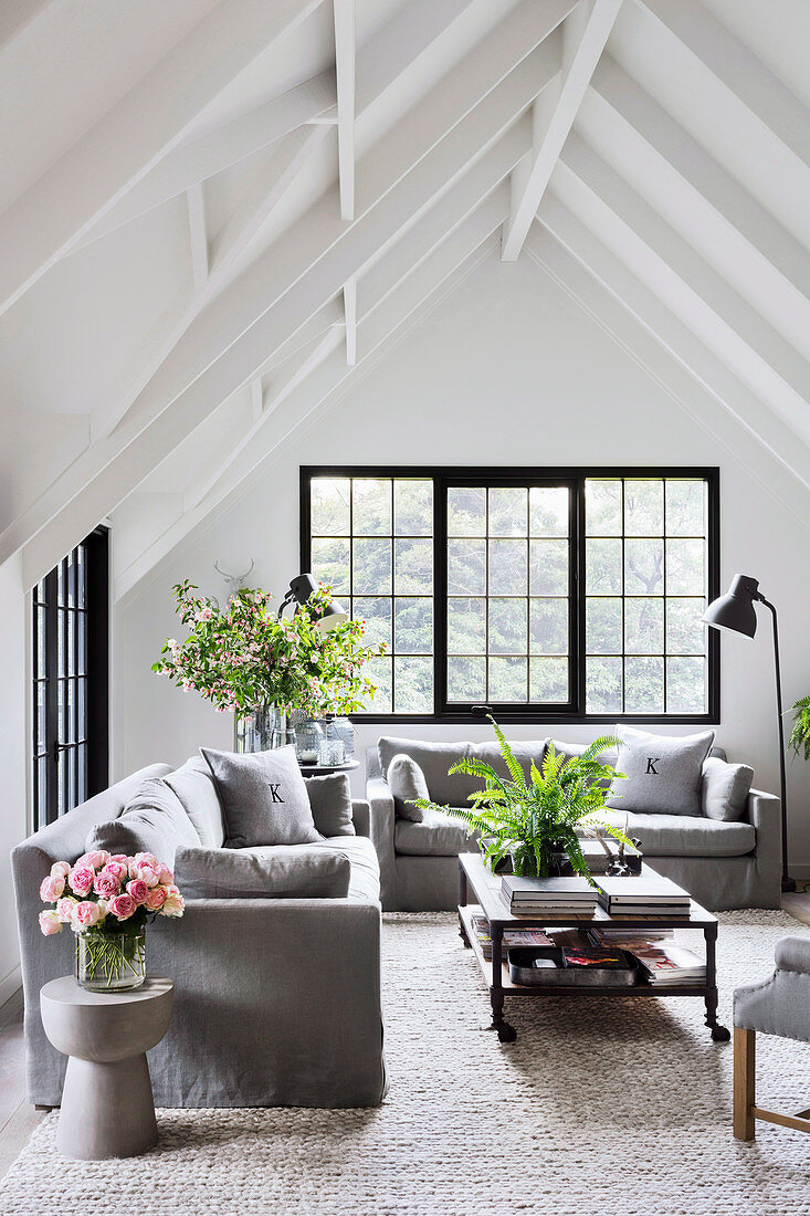 Bright living room under white gable roof with grey sofas and black mullioned windows