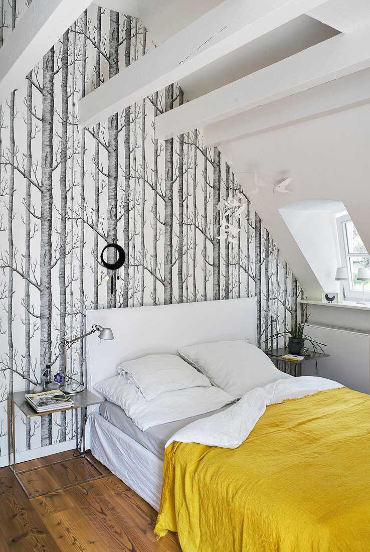 Bed under sloping ceiling and against wall with forest-motif wallpaper