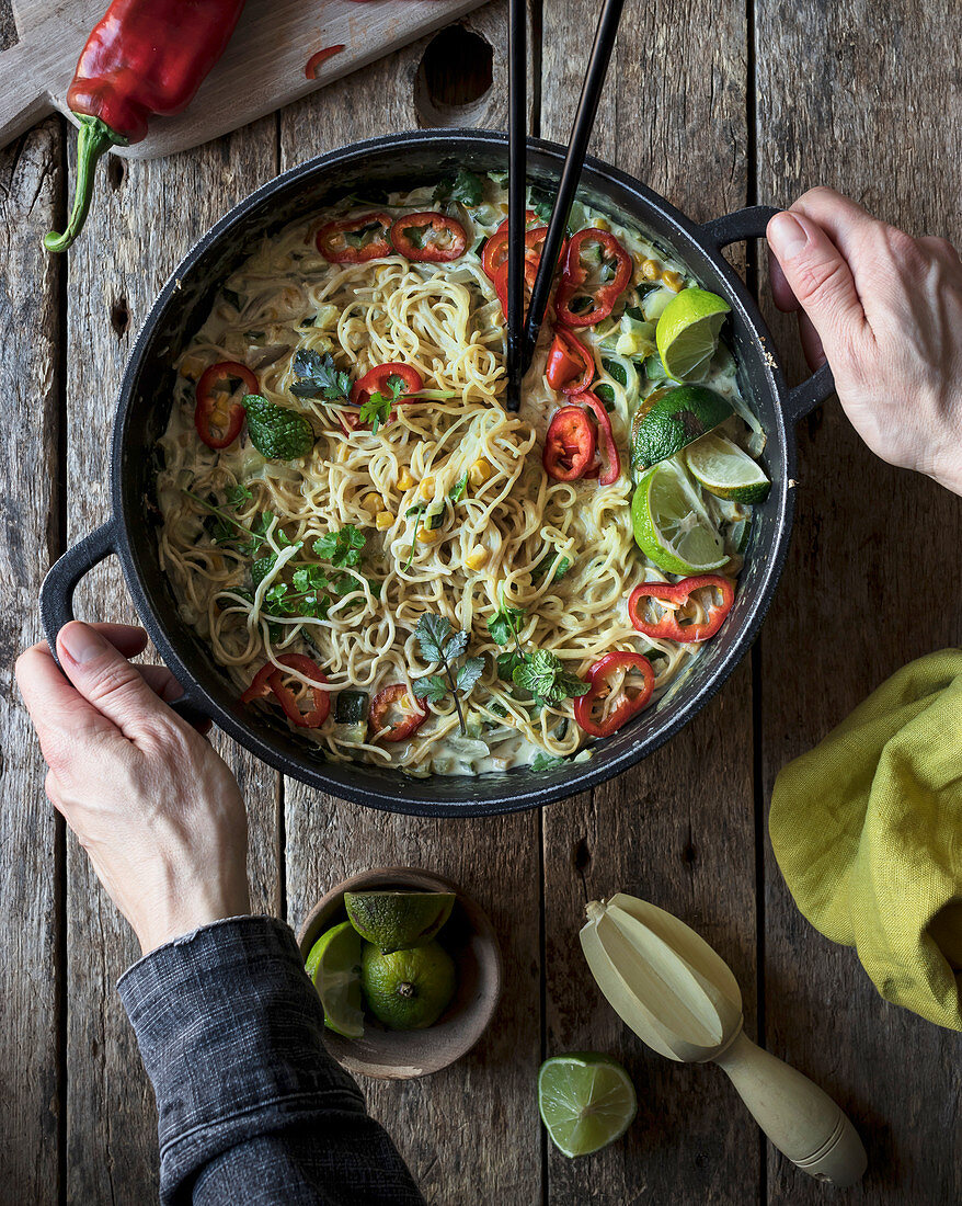 Green curry pasta with limes, herbs and chili pepper in pot on wooden background