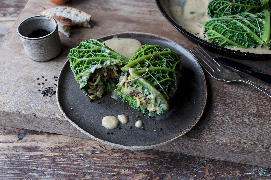 Cabbage leaves stuffed with rice on plate near pan, slice of bread and fork on wooden background