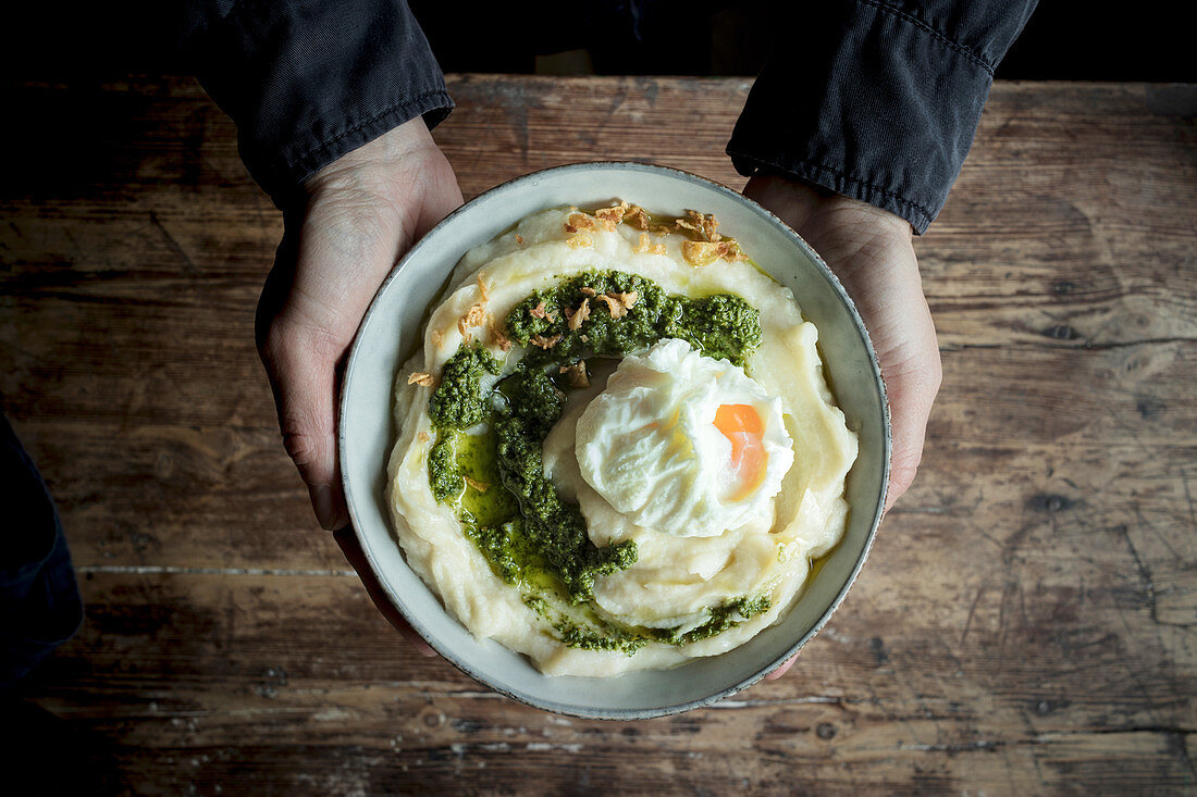 Hands holding bowl with cauliflower puree with pesto and eggs