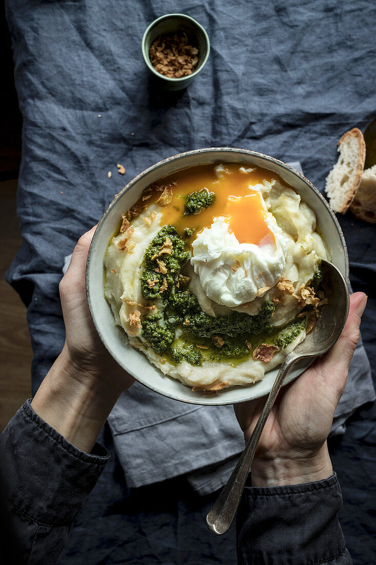 Hände halten eine Schüssel Blumenkohlpüree mit Pesto und pochiertem Ei