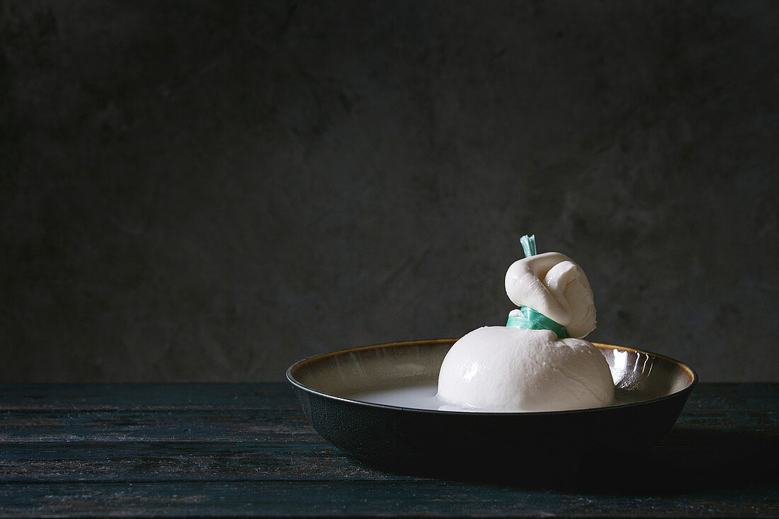 Bowl with whole tied Italian cheese burrata in brine on wooden plank table