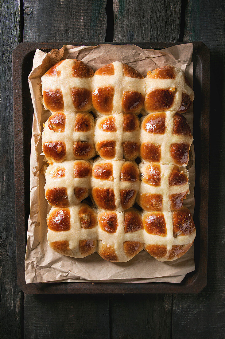Homemade Easter traditional hot cross buns on oven tray with baking paper over dark wooden background