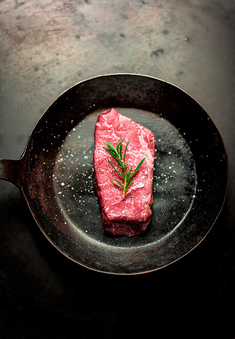 A beef steak with rosemary in a pan