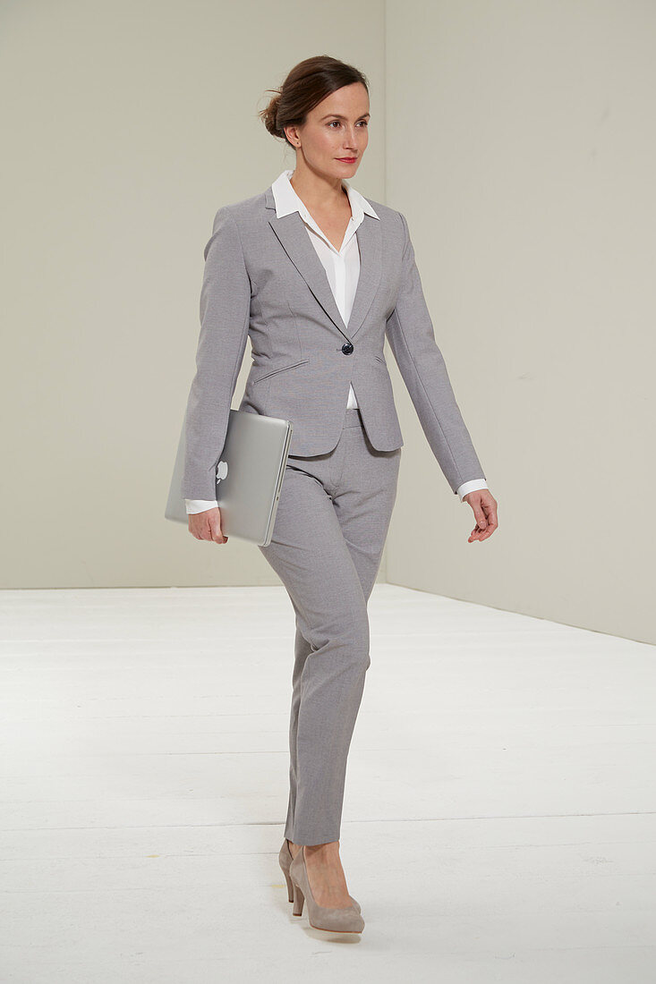 A woman wearing a grey trouser suit with a laptop