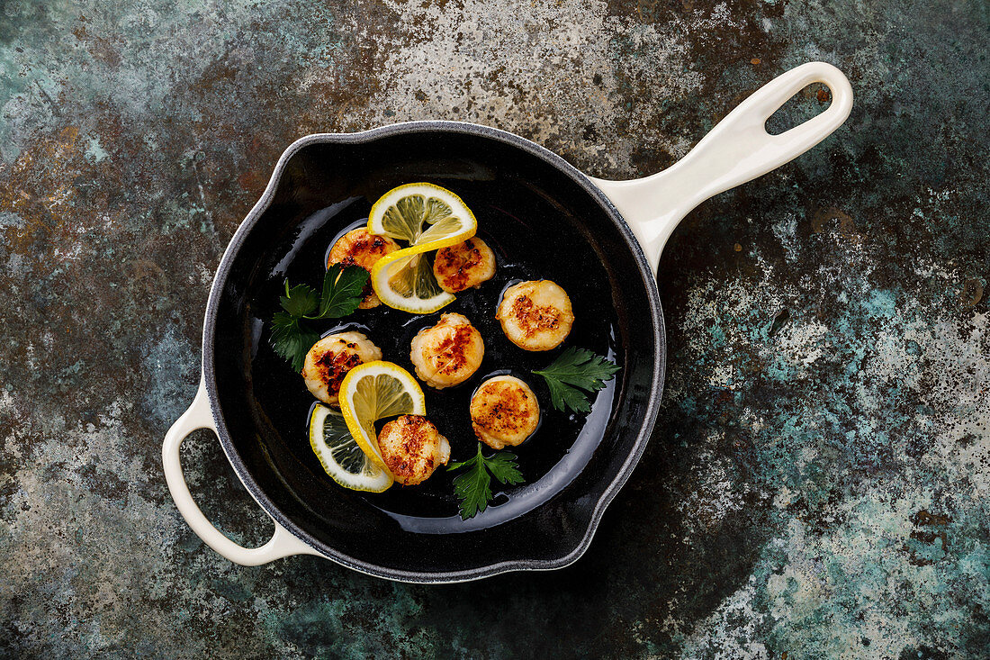 Fried scallops with butter in cast-iron cooking pan with lemon and leaf vegetable
