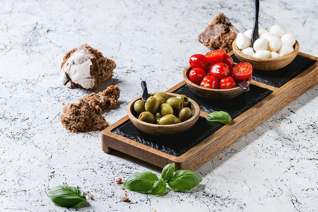 Mozzarella, cherry tomatoes, olives antipasto appetizers served in wooden bowl