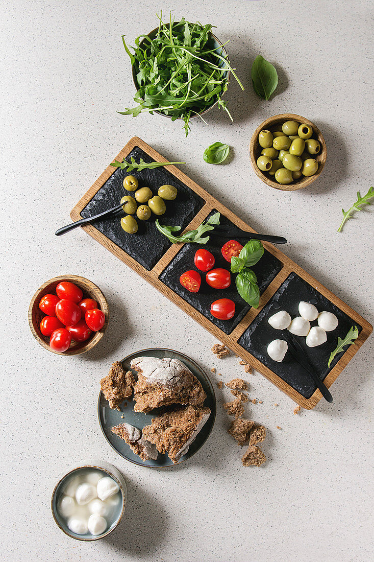 Antipasti mit Mozzarella, Kirschtomaten, Oliven, Brot und Rucola