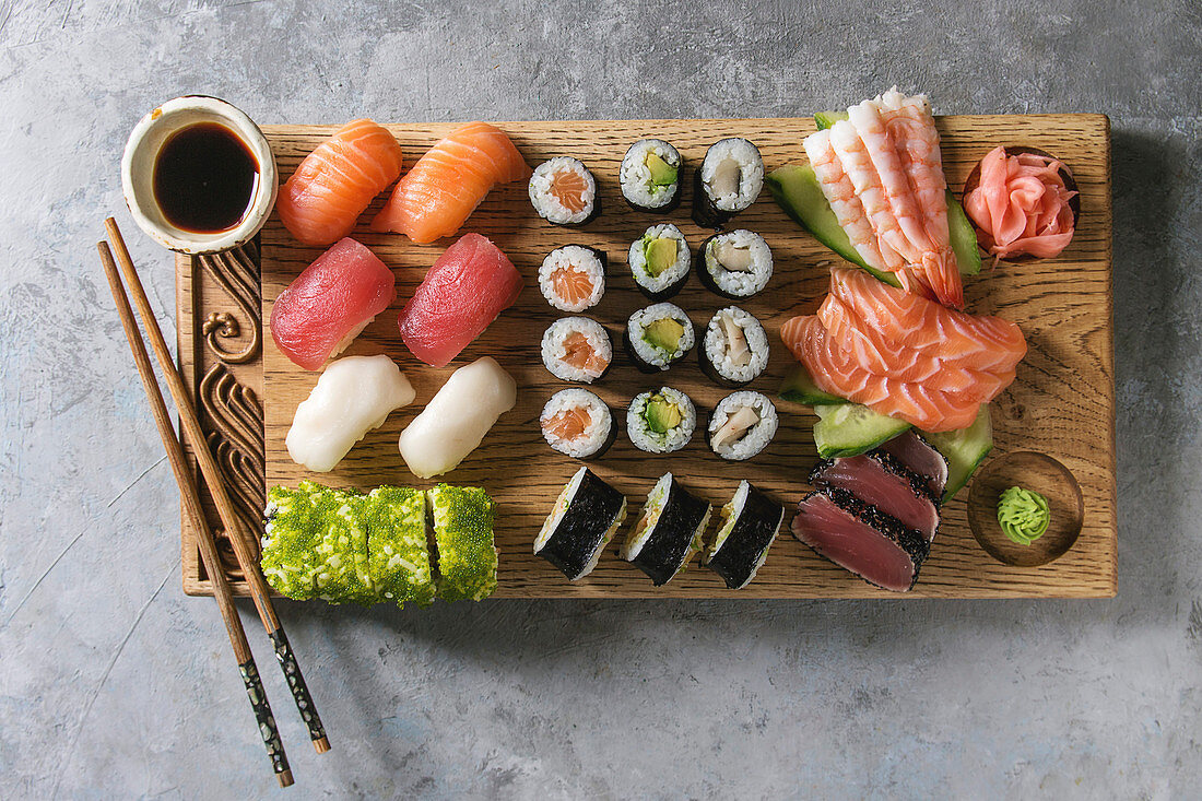 Sushi Set: nigiri, sashimi and sushi rolls on wooden serving board with soy sauce and chopsticks