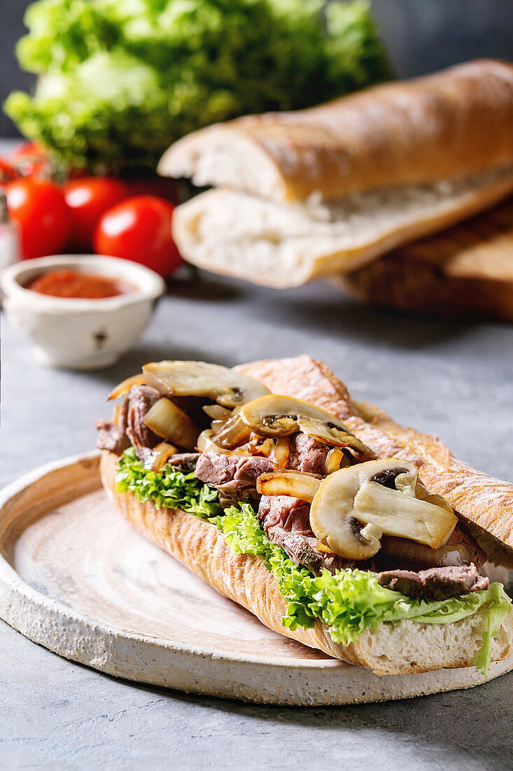 Beef baguette sandwich with champignon mushrooms, green salad and fried onion
