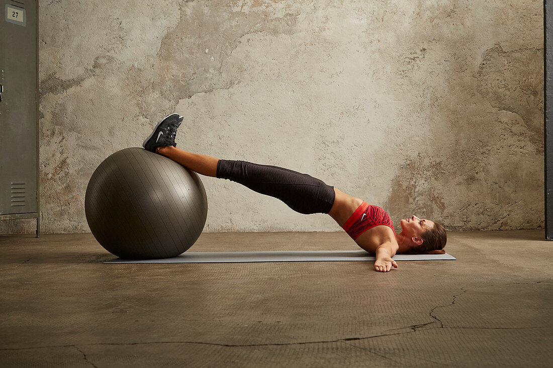 A young woman lying on her back performing an exercise with on a gym ball