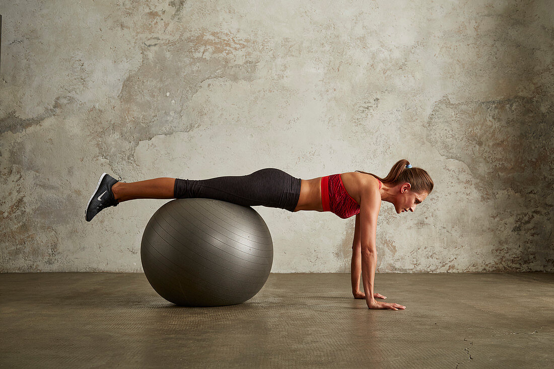 A young woman performing push-ups with her legs on a gym ball